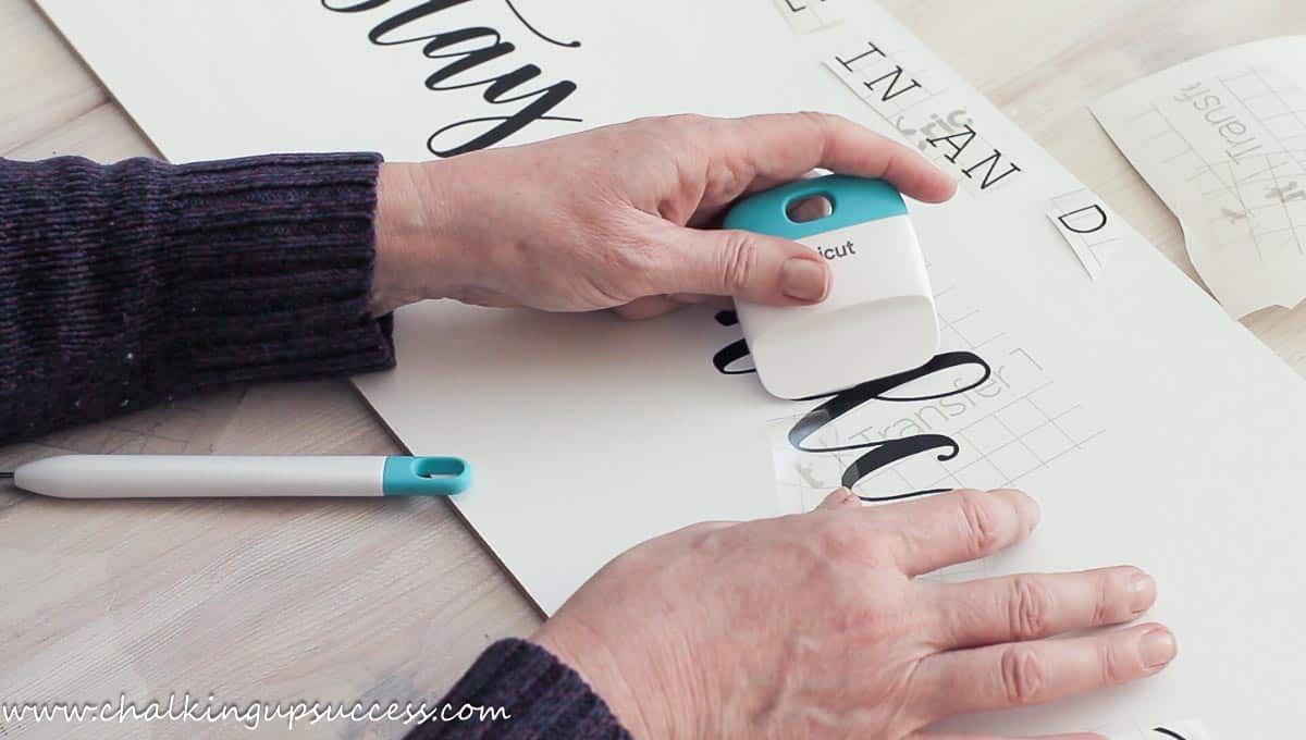 Applying the Cricut text to the DIY farmhouse sign using a scraper tool.