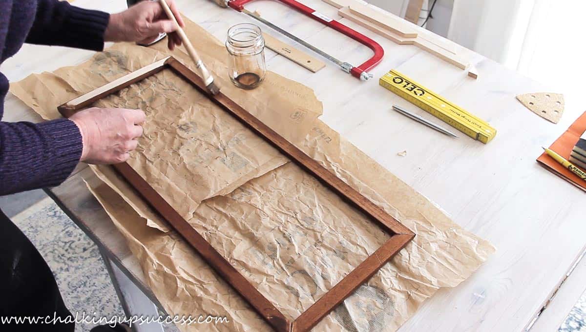 Using a paintbrush to apply Walnut wood stain to a DIY frame.