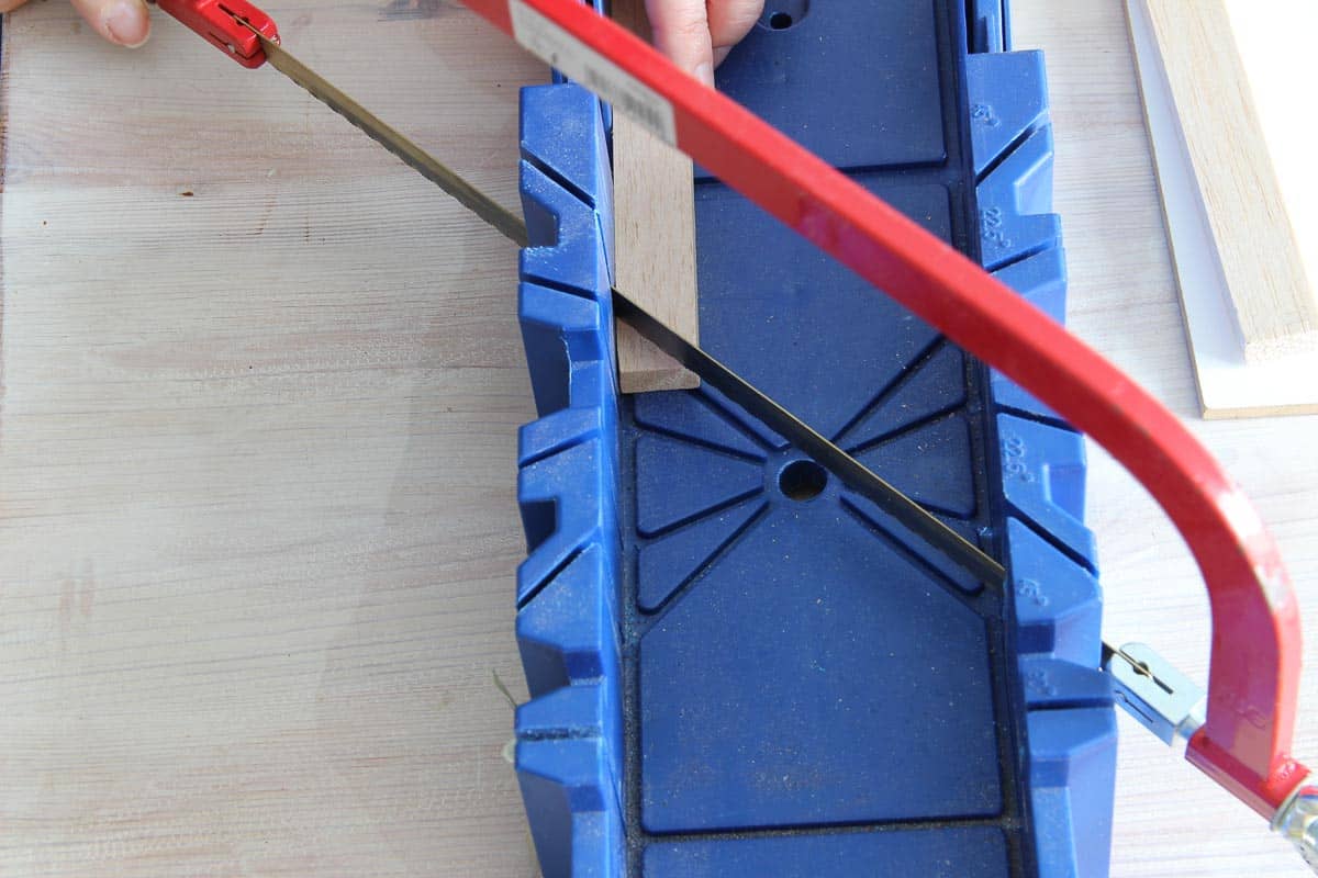 Cuttingg the DIY frame pieces pieces at a 45° angle using a hand saw and miter box.