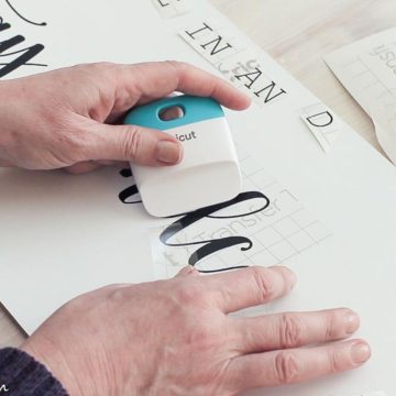 Using a Cricut scraper tool to transfer text to a DIY farmhouse sign.