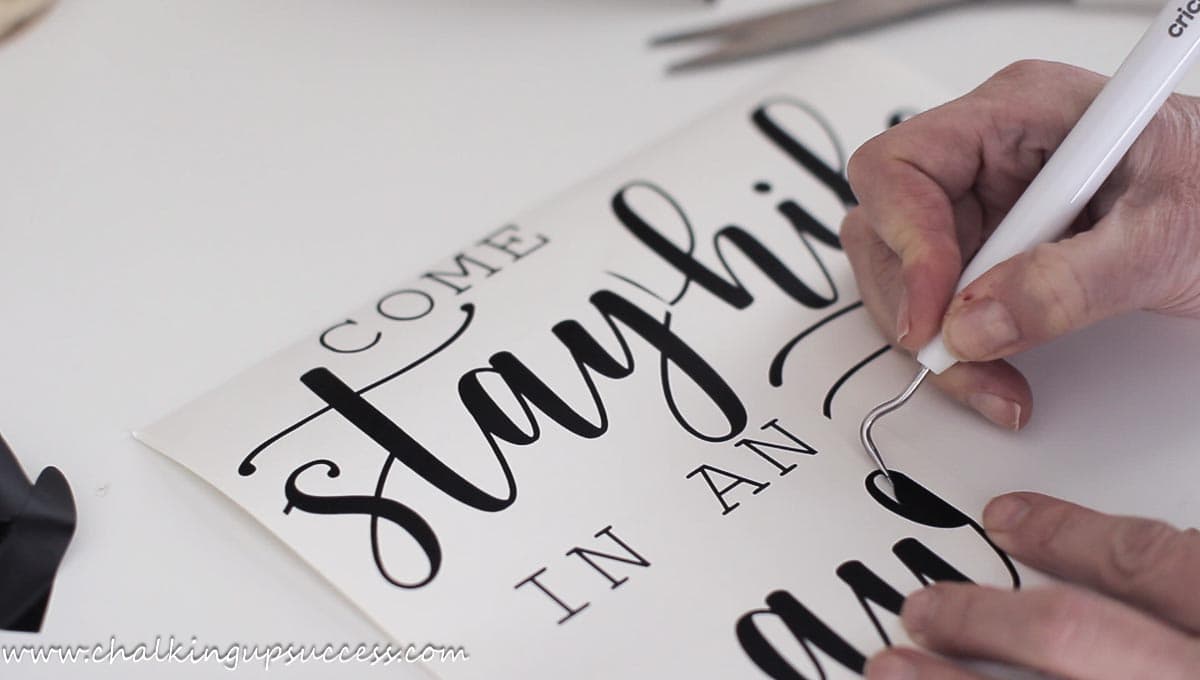 Using a Cricut weeding tool to remove unwanted vinyl from text for a farmhouse sign.