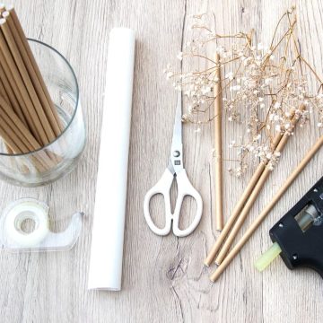 Supplies for making baby's breath centerpieces. A glass vase, straws, paper, sand, tape, scissors, glue, and gypsophilia.
