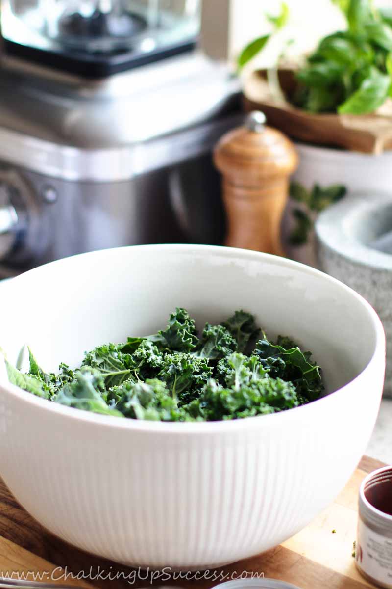 Get the Kale chips recipe on my blog at Chalking Up Success dot com Bite-size pieces of kale in a white bowl, ready for seasoning.
