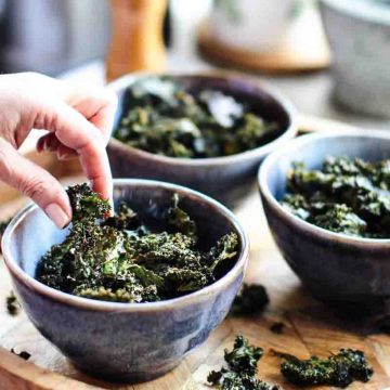 A hand picking crispy kale chips out of a bowl