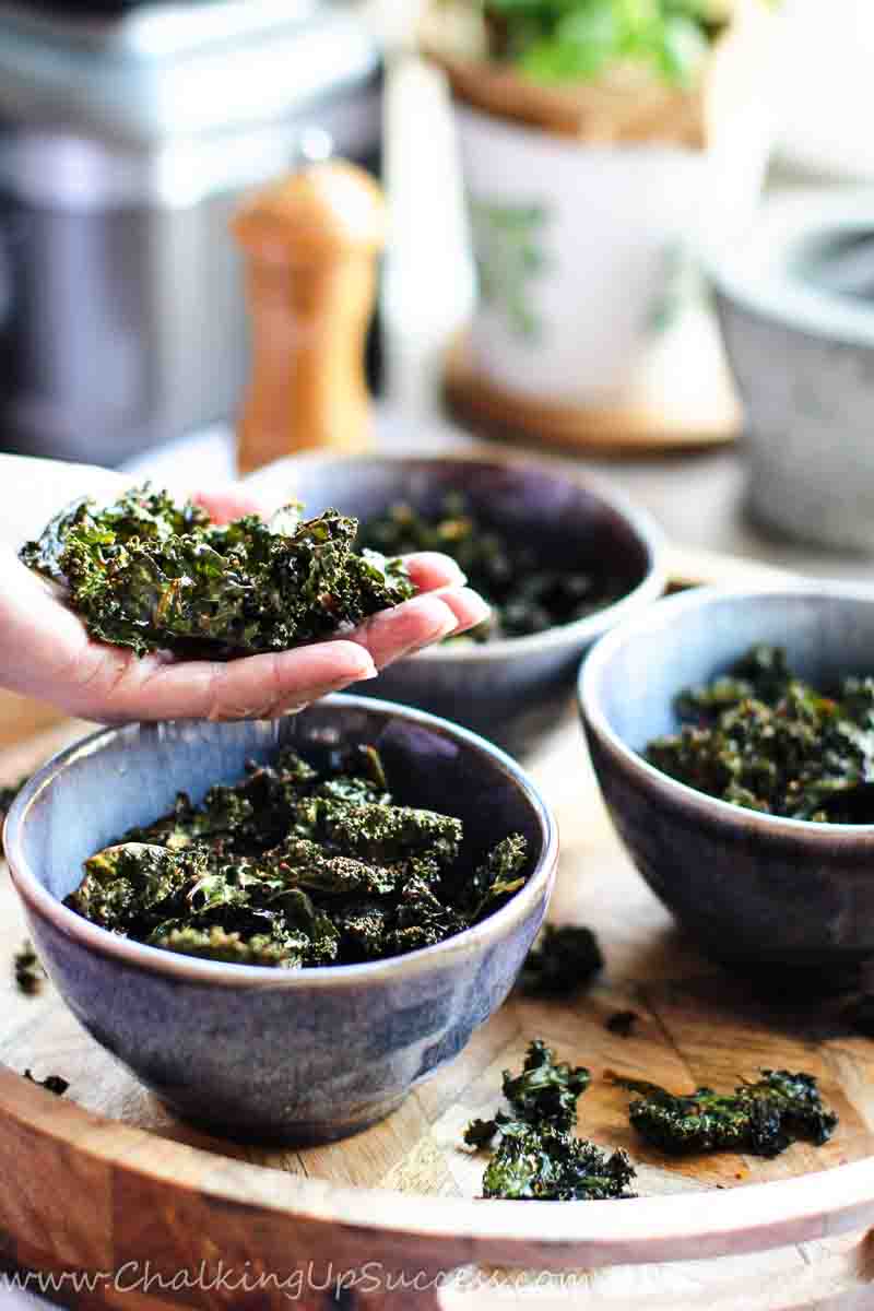Get the Kale chips recipe on my blog at Chalking Up Success dot com A pile of kale chips in the palm of a hand